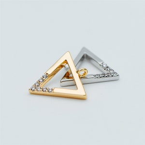 Pode incluir: Dois pingentes em forma de triângulo com acabamento dourado e prateado. Ambos os pingentes são adornados com strass transparentes ao redor das bordas.