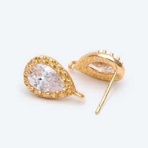 May include: A pair of gold teardrop earrings with clear cubic zirconia stones. The earrings have a delicate, ornate design and are perfect for adding a touch of sparkle to any outfit.