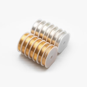 May include: Two spools of wire, one gold and one silver, are wrapped around white plastic spools. The spools are stacked on top of each other.