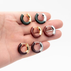 May include: A collection of hoop earrings in various color combinations. The earrings feature a gold, silver, and dark green or brown color scheme. The earrings are small and circular, with a hinged closure.