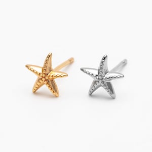 May include: Two starfish stud earrings, one gold-toned and one silver-toned, are displayed on a white background. The earrings are detailed with textured surfaces, and each has a post for piercing.