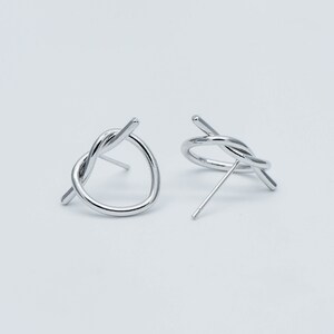 May include: A pair of silver knot earrings with a twisted wire design. The earrings are simple and modern.