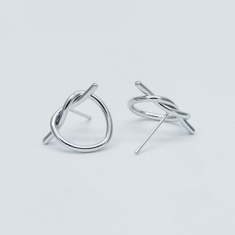 May include: A pair of silver knot earrings with a twisted wire design. The earrings are simple and modern.