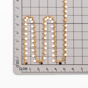 May include: A gold chain necklace with small round discs hanging from it. The chain is measured on a ruler in centimetres.