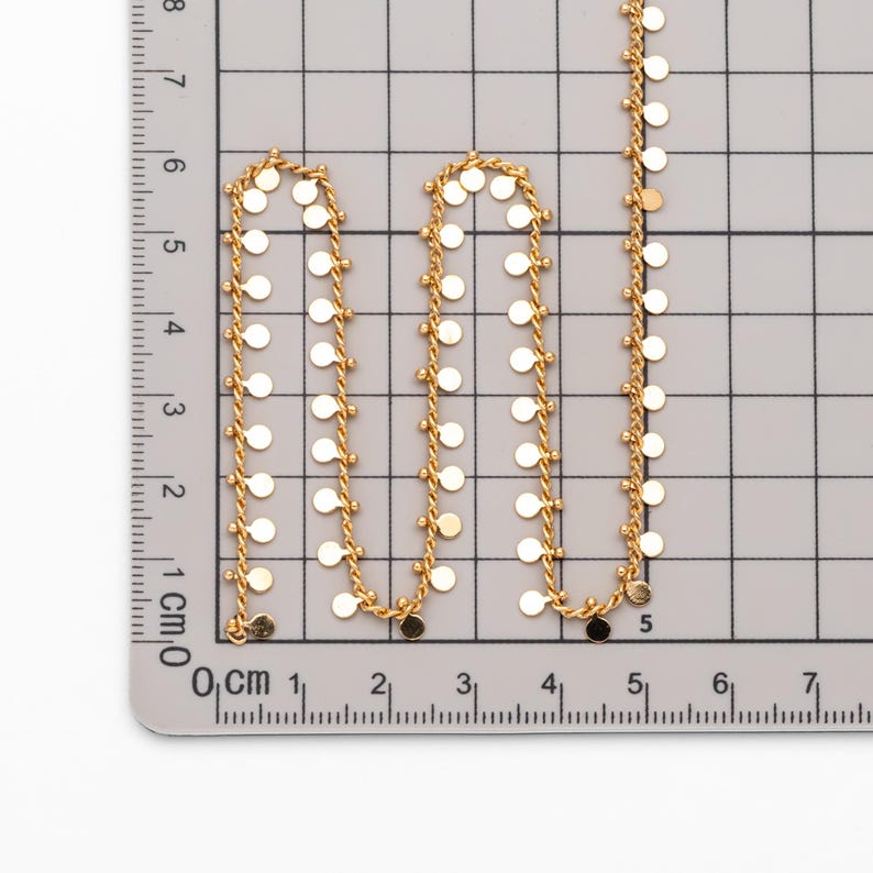 May include: A gold chain necklace with small round discs hanging from it. The chain is measured on a ruler in centimetres.