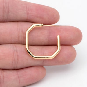 May include: Gold octagon hoop earrings. The earrings are simple and modern, with a smooth finish.