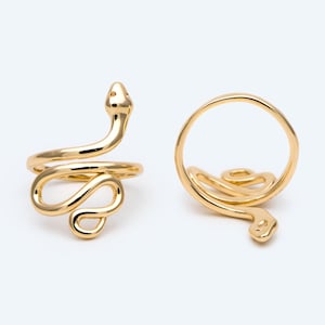 May include: Two gold-coloured snake rings. One ring is shown from the side, with the snake's head and body wrapping around the finger. The other ring is shown from above, with the snake's head and body forming a loop. The rings are on a white background.