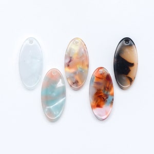 May include: Five oval-shaped resin pendants with a hole at the top for hanging. The pendants are in various colors and patterns, including white, blue, orange, and brown.
