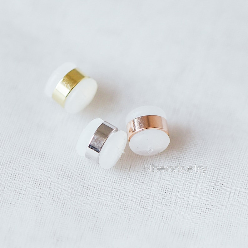 May include: Three white round beads with a metal band around the middle. The beads are gold, silver, and rose gold.