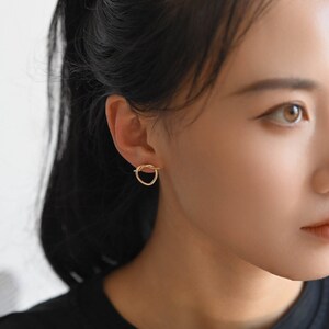 May include: A close-up of a person's ear with a gold, knotted circle earring.