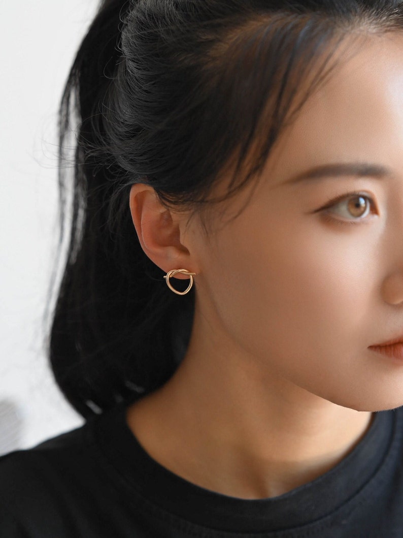 May include: A close-up of a person's ear with a gold, knotted circle earring.