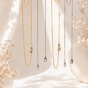 May include: A collection of delicate metal chains hanging vertically, featuring both gold-toned and silver-toned finishes. Each chain includes small circular links, integrated lobster claw clasps, and adjustable segments for length customization.
