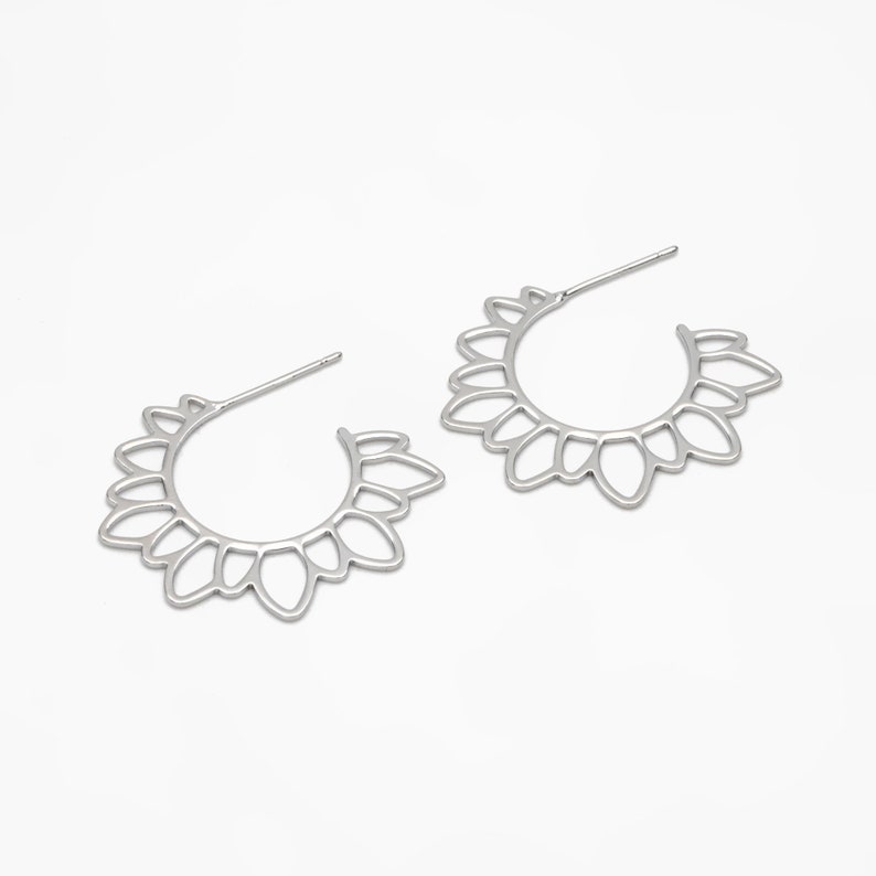 Puede incluir: Un par de pendientes de aro plateados con un delicado dise&ntilde;o floral. Los pendientes est&aacute;n hechos de metal y tienen una forma circular.