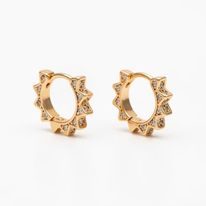 May include: A pair of gold hoop earrings with a starburst design. Each earring is adorned with small, clear cubic zirconia stones.