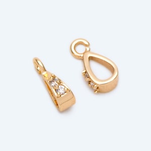 May include: Two gold-tone pendant bails with clear crystal accents. The bails are shaped like teardrops and have a loop at the top for attaching a chain.