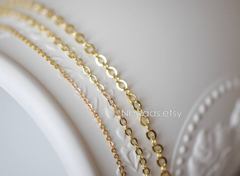 May include: Three gold chains of different sizes and thicknesses, displayed on a white surface. The chains are made of small, oval-shaped links.