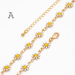 Könnte beinhalten: Goldfarbene Gliederkette mit Gänseblümchen mit weißen Blütenblättern und gelben Zentren. Die Halskette hat eine verstellbare Kette und einen Karabinerverschluss. Der Buchstabe "A" ist im Bild sichtbar.