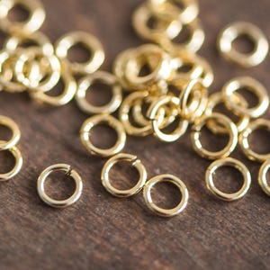 May include: A close-up of a pile of gold jump rings. The rings are small and round, and they are all made of the same metal. They are perfect for jewelry making or other crafting projects.