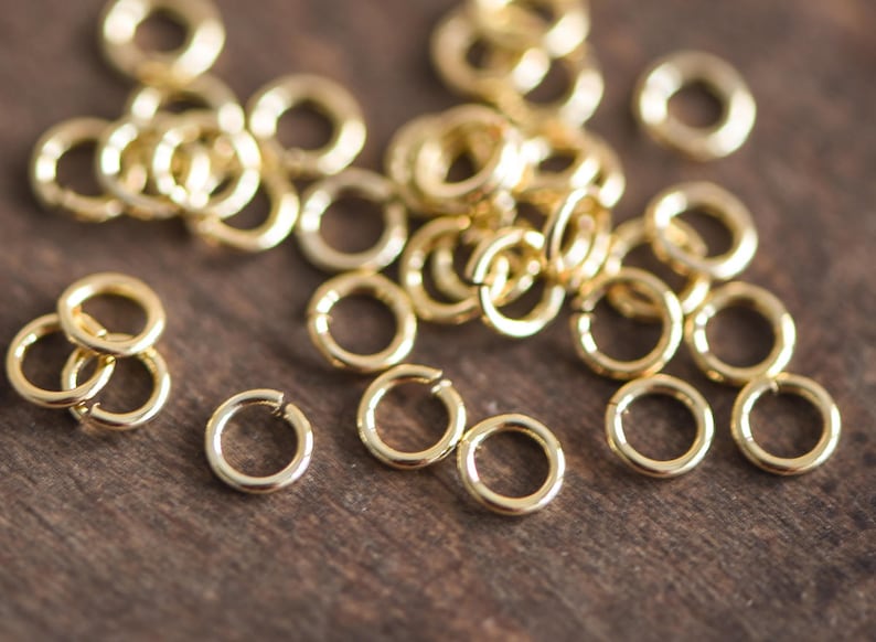 May include: A close-up of a pile of gold jump rings. The rings are small and round, and they are all made of the same metal. They are perfect for jewelry making or other crafting projects.