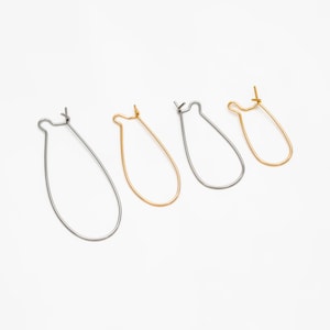 May include: Four earring hoops, two silver and two gold, are arranged in a row on a white surface. The hoops are all the same size and shape, but they are different colours.