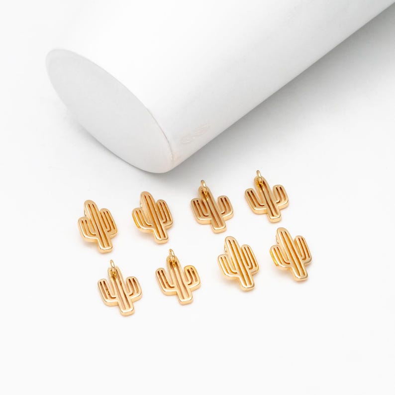 Op de afbeelding: Negen goudkleurige metalen cactusbedels. De bedels zijn klein en gedetailleerd, met een eenvoudig ontwerp.
