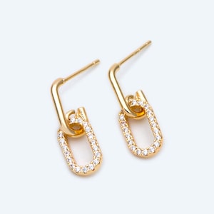 May include: A pair of gold earrings with a linked chain design. Each earring features a small oval shape with clear cubic zirconia stones.