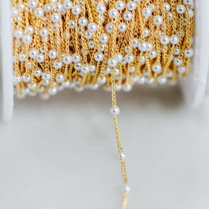 May include: A spool of gold chain with white pearl beads. The chain is strung with small, evenly spaced pearls.
