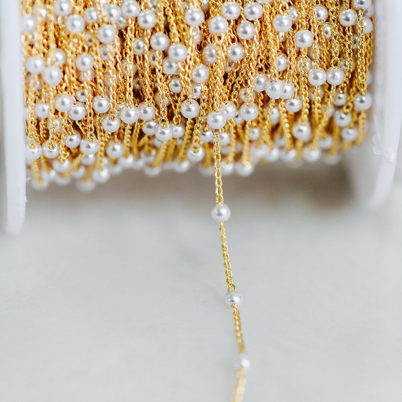 May include: A spool of gold chain with white pearl beads. The chain is strung with small, evenly spaced pearls.