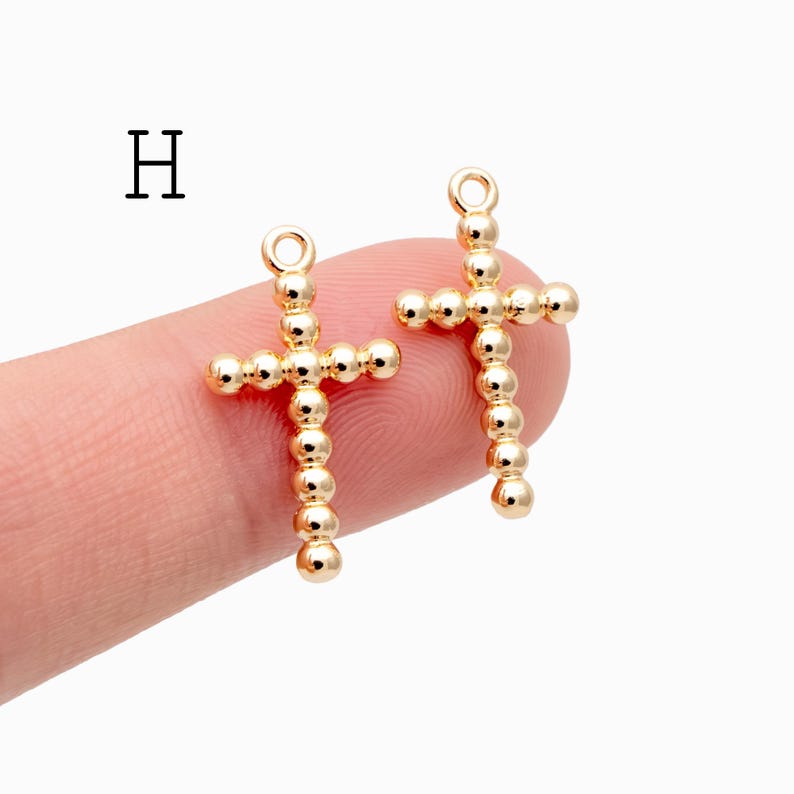 Pu&ograve; includere: Due ciondoli a forma di croce color oro. Ogni croce &egrave; composta da piccole perline rotonde. Le croci hanno un anello nella parte superiore per il fissaggio a una catena o ad un altro componente di gioielleria. La lettera "H" &egrave; nell'angolo in alto a sinistra.