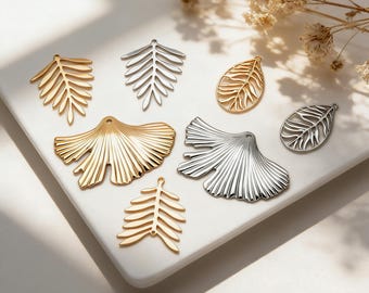 May include: A collection of metal jewelry charms in gold and silver tones. The set includes fern-shaped pieces, ginkgo leaf-shaped charms, and teardrop-shaped leaf pendants, each featuring a small loop at the top for attachment.