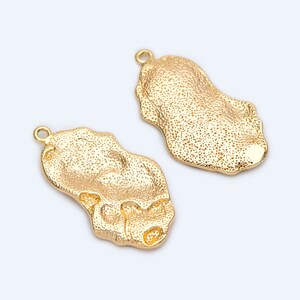 May include: Two gold-toned metal charms shaped like irregular ovals with a textured surface. Each charm has a small loop at the top for attaching to jewellery.