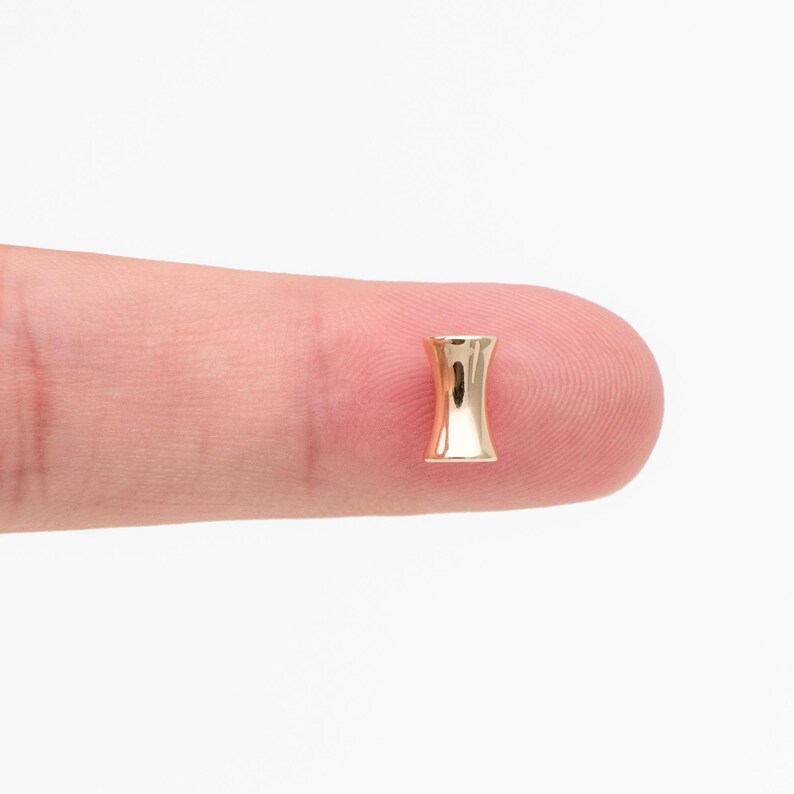 May include: A gold-colored metal ear gauge with a flared design. The gauge is shown on a finger.