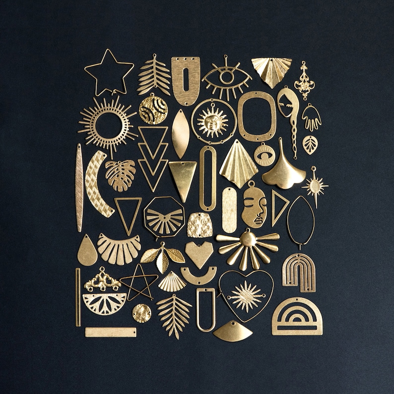 May include: A collection of gold-toned metal earring charms in various shapes, including stars, suns, leaves, geometric shapes, and abstract designs.