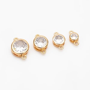 Op de afbeelding: Vier goudkleurige connector charms met heldere ronde strass steentjes. De charms hebben twee lussen aan de zijkant om aan sieraden te bevestigen.