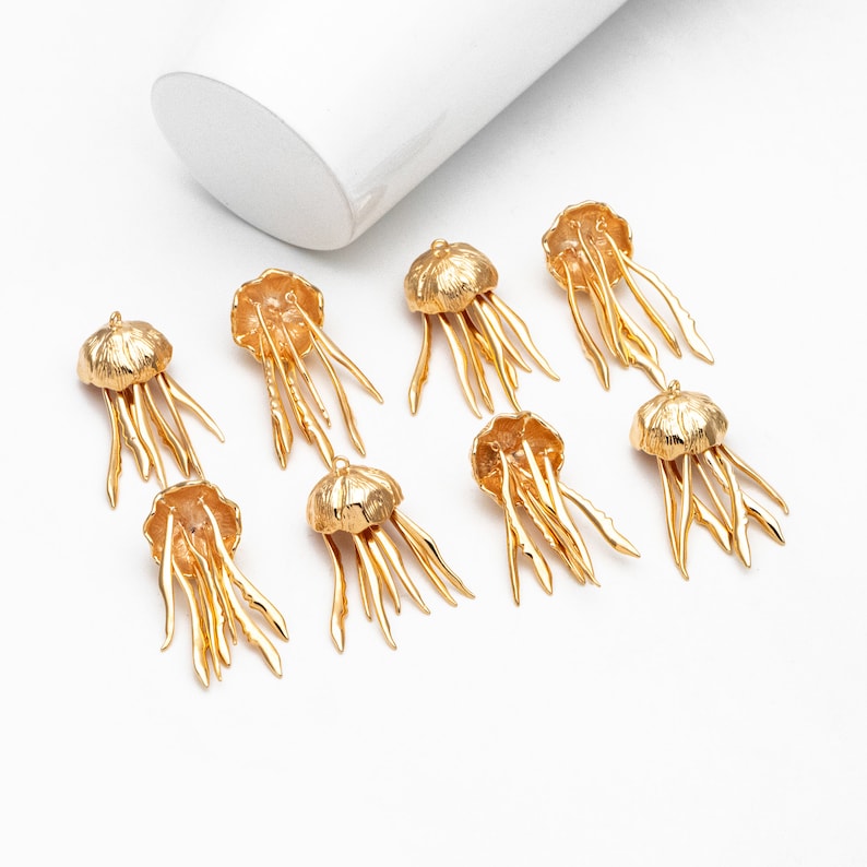 May include: Ten gold-colored metal jellyfish charms with intricate details. Each charm features a domed top and multiple tentacles.