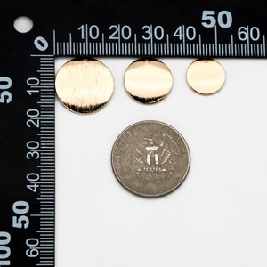 May include: Three gold-colored metal discs of varying sizes, with a brushed finish. The discs have a hole in the top and are shown next to a US quarter for size comparison.