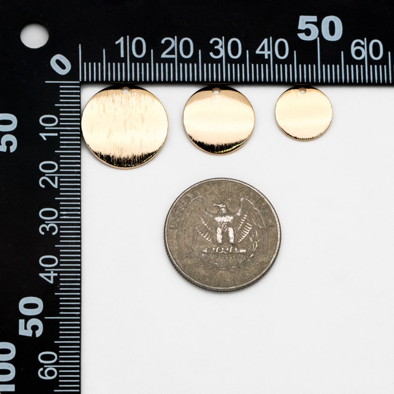 May include: Three gold-colored metal discs of varying sizes, with a brushed finish. The discs have a hole in the top and are shown next to a US quarter for size comparison.