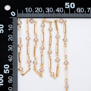 May include: Gold chain with small white pearl accents. The chain is made of rectangular and square links.