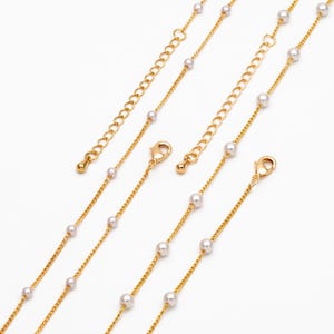 Puede incluir: Collares dorados con pequeñas perlas blancas. Los collares tienen un diseño de cadena delicado con un cierre de mosquetón y una cadena extensora. El fondo es blanco.