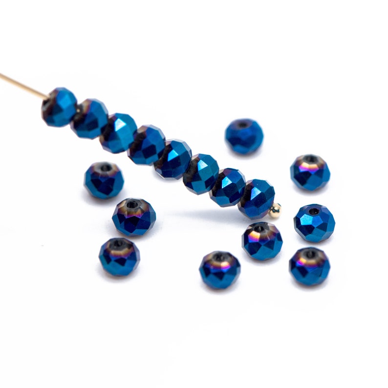 Pu&ograve; includere: Perline blu iridescenti sfaccettate, alcune infilate su un sottile filo d'oro, altre sparse. Le perline hanno una lucentezza metallica e un design sfaccettato che riflette la luce. Ideali per la creazione di gioielli.