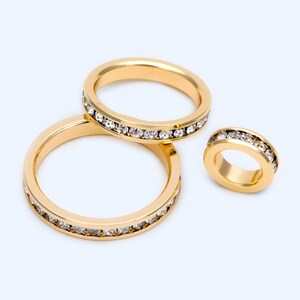 May include: Three gold rings with a row of clear rhinestones around the edge. The rings are different sizes.