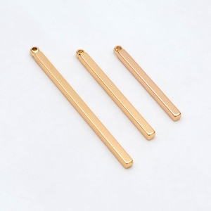 May include: Three gold-colored metal bars with a loop at the top. The bars are different lengths and are arranged in descending order of size.
