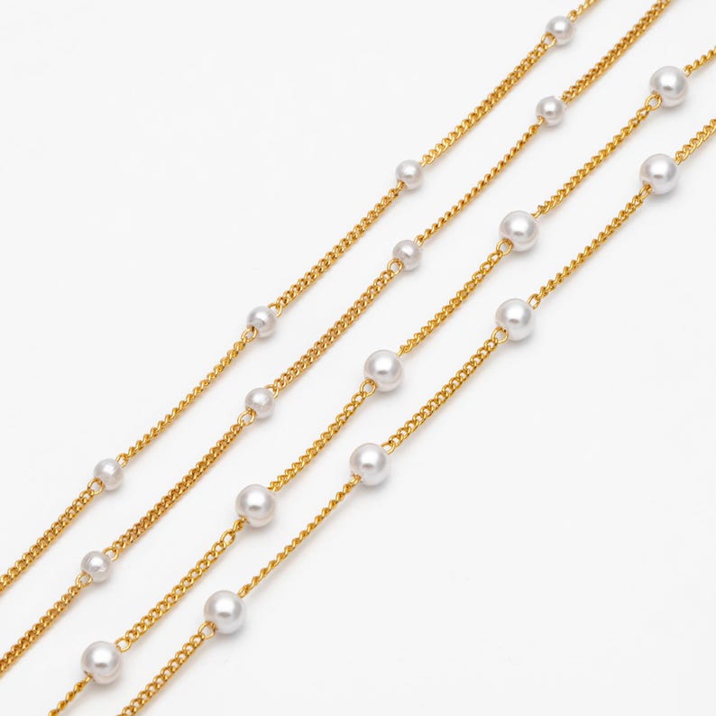 May include: Four gold chains with white pearl accents. The chains are layered on a white background.