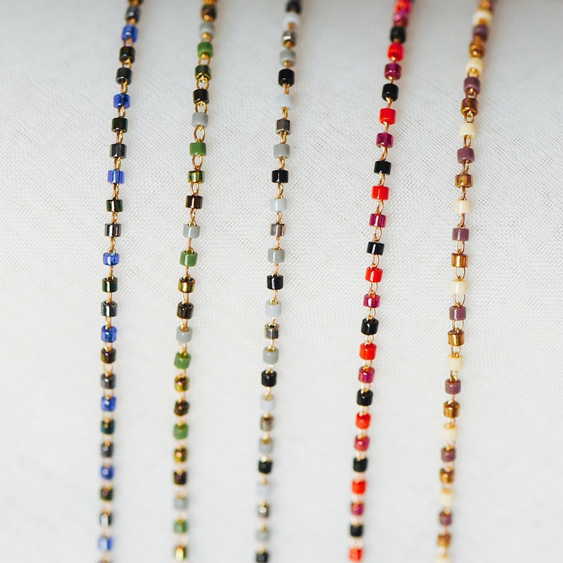 May include: Seven strands of gold chain necklaces with different colored beads. The beads are small and square shaped. The colors of the beads are blue, green, gray, black, red, brown, and white.