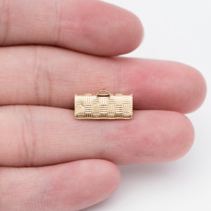 Puede incluir: Un peque&ntilde;o cierre de joyer&iacute;a dorado con un patr&oacute;n de cesta tejida. El cierre tiene forma rectangular con un peque&ntilde;o lazo en la parte superior. El cierre se sostiene en la mano de una persona sobre un fondo blanco.