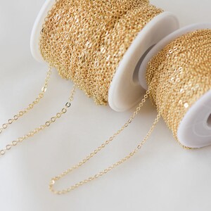 May include: Two spools of gold chain, one on top of the other. The chain is a delicate, fine link style. The chain is unwound and laid out on a white surface.