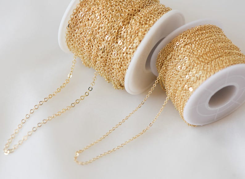 May include: Two spools of gold chain, one on top of the other. The chain is a delicate, fine link style. The chain is unwound and laid out on a white surface.