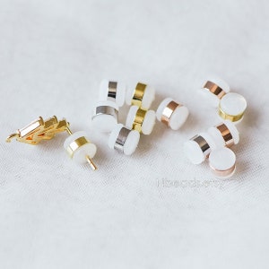 May include: Assortment of earring backs in gold, silver, and rose gold finishes. The backs are made of metal and have a clear plastic backing.