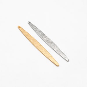 Puede incluir: Dos formas metálicas planas y alargadas con un agujero en la parte superior. Una es dorada y la otra es plateada.