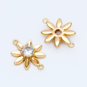 May include: Two gold-tone flower-shaped charms with a clear rhinestone in the center. One charm has two loops on the side, the other has one loop on the side.